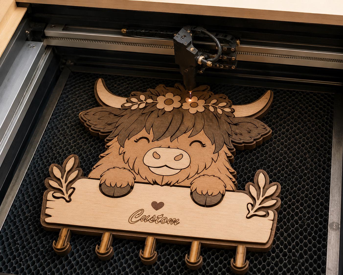 Laser machine engraving a personalized Highland Cow key holder laser cut file made from layered plywood, ready for Glowforge and CNC projects.