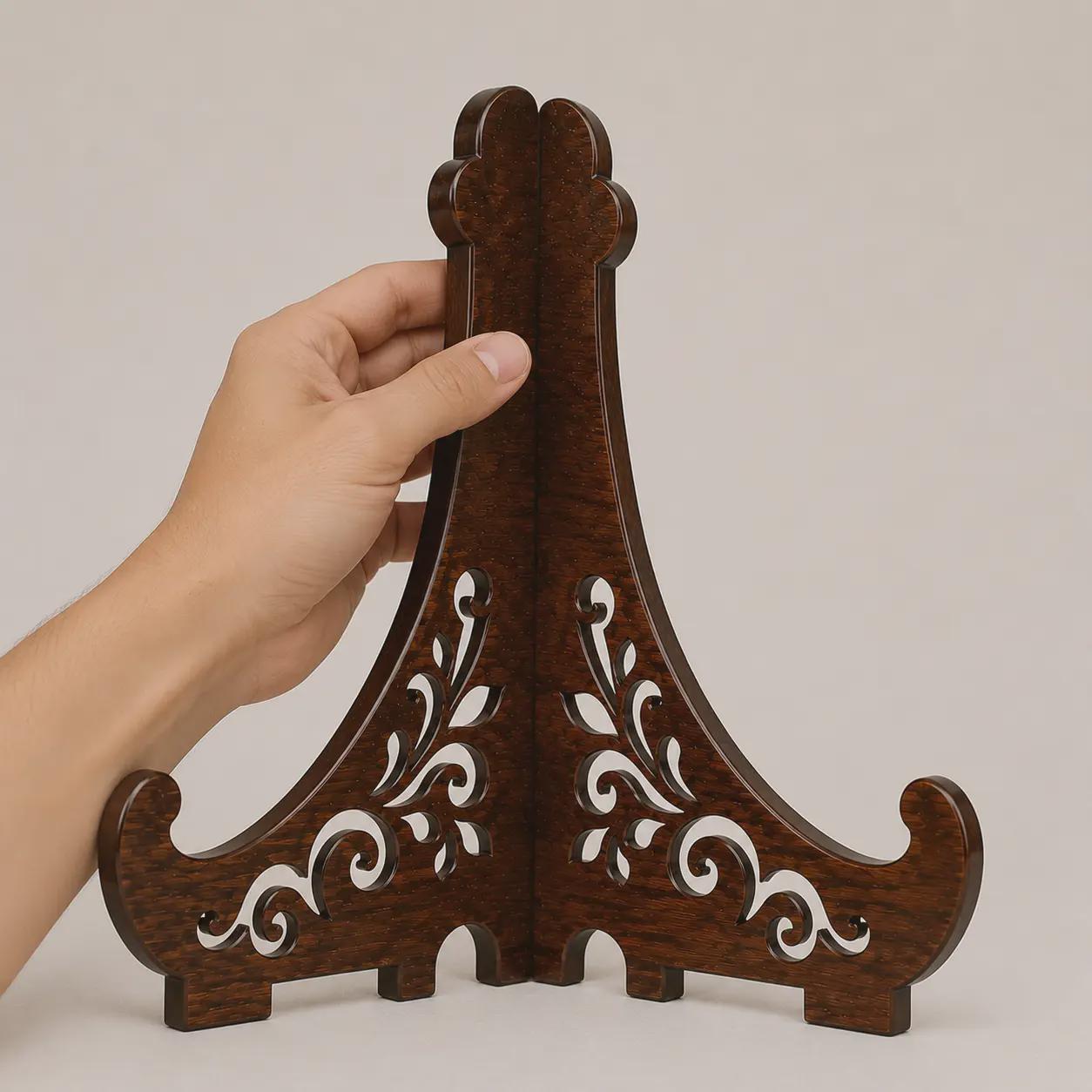 Hand holding assembled laser cut easel stand for size reference, showcasing decorative wooden construction, floral scroll pattern, and display holder functionality.