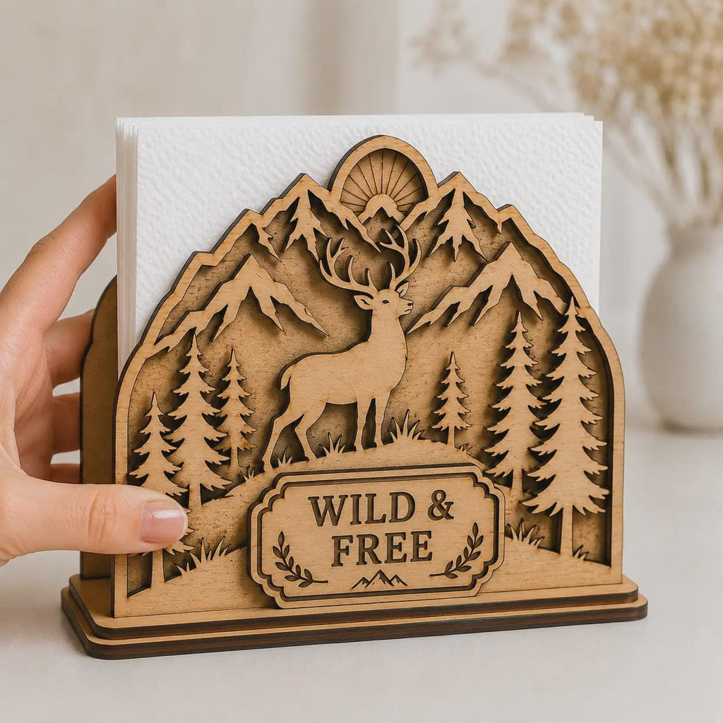 Side-angle view of a layered wooden napkin holder with deer, mountain landscape, pine trees, and Wild & Free engraving designed for laser cutting and home decor.