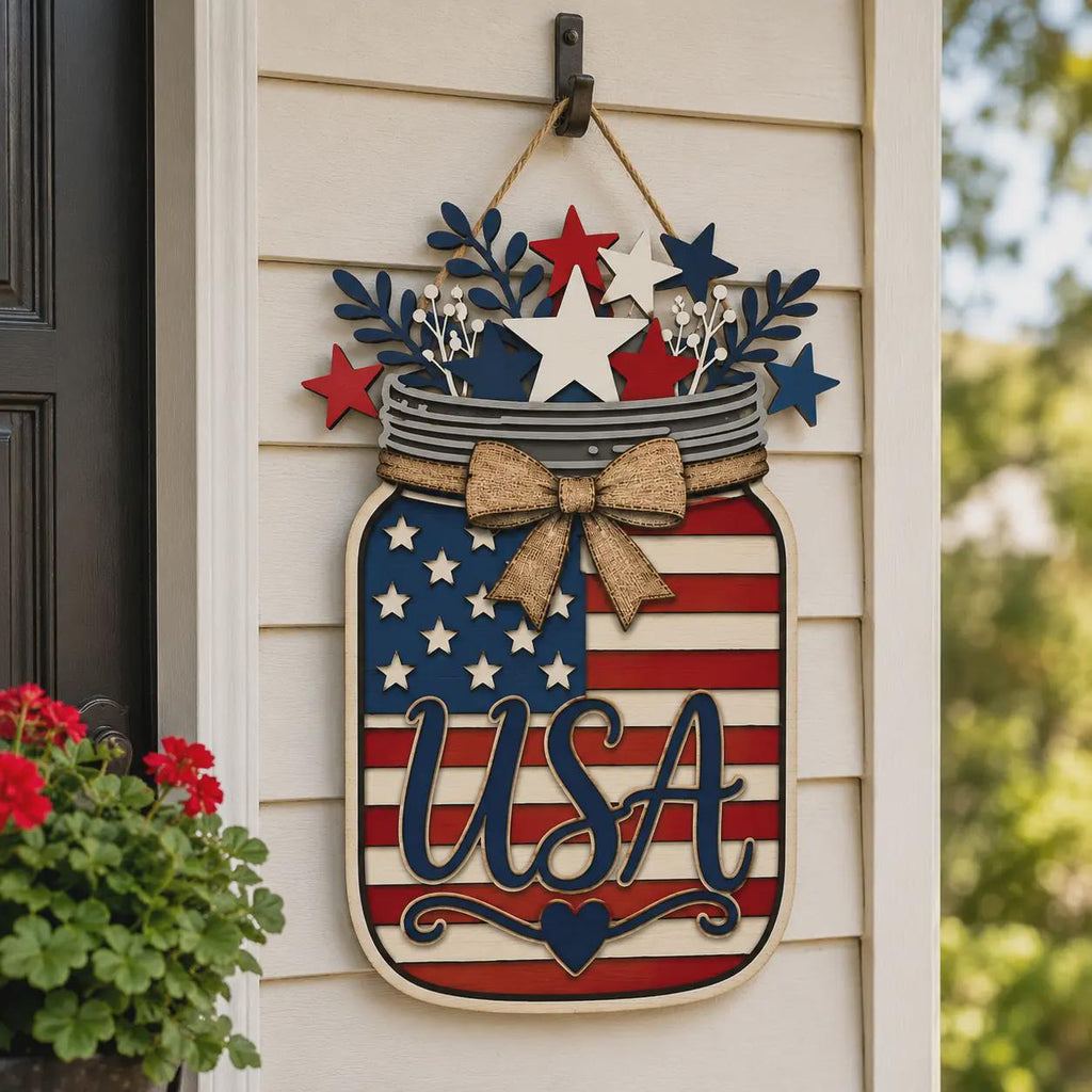 Patriotic American Flag Mason Jar wall hanging with USA lettering, stars, stripes, and rustic bow displayed on an exterior porch wall for Independence Day decor.