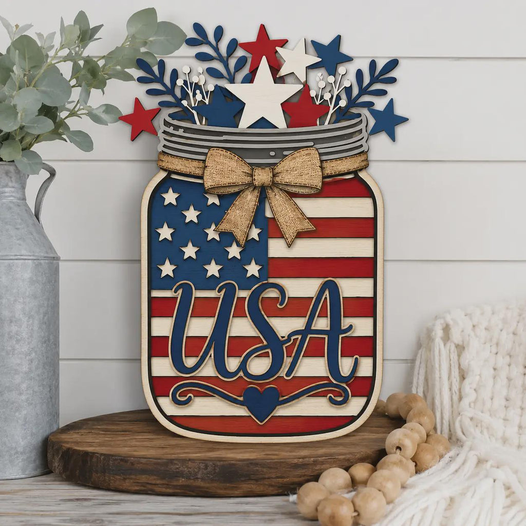 Patriotic USA Mason Jar wooden sign displayed on a farmhouse shelf, layered American flag laser cut design with stars, bow, and Independence Day home decor styling.